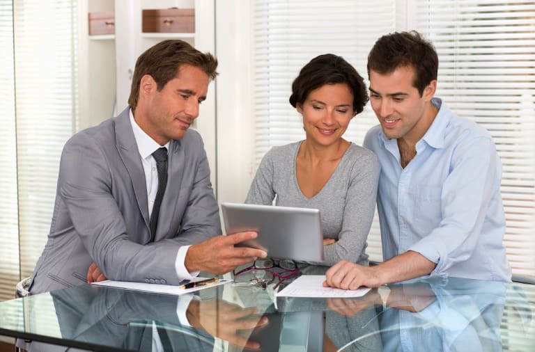 Three people sitting at a table looking at a tablet.