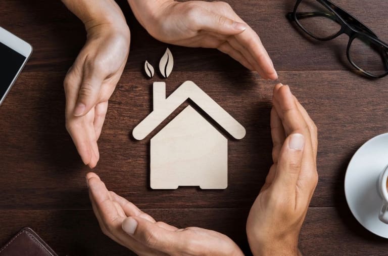 A group of people holding hands around a wooden house.